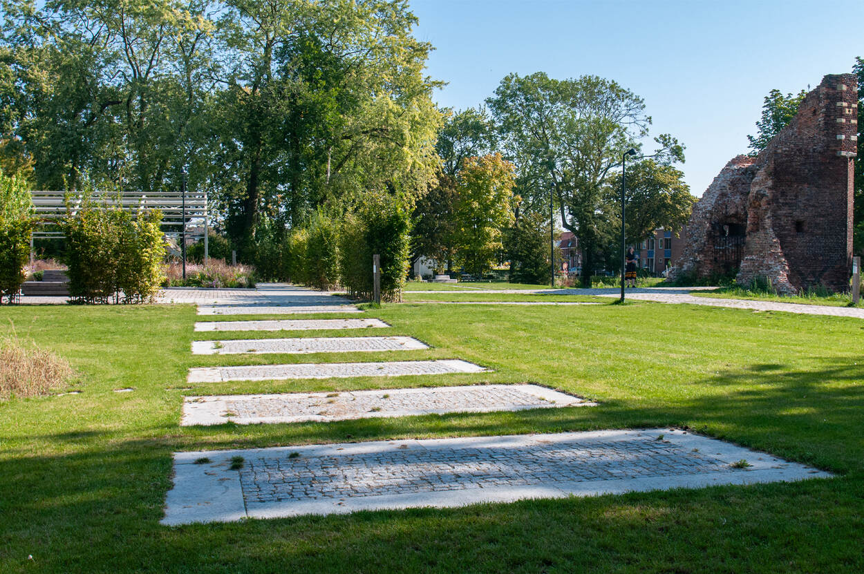 Een blik op Kasteelpark Nijeborg, met op de voorgrond in het gras een aantal grijze, rechthoekige stenen die de vorm van de brug over de slotgracht aangeven.