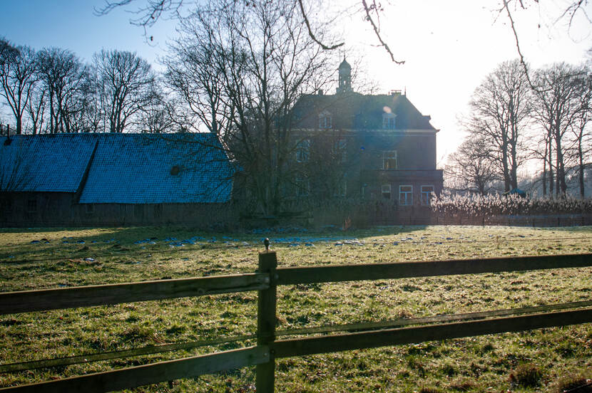 Winters uitzicht op het landhuis van landgoed 't Medler met op de voorgrond bomen en een hek.