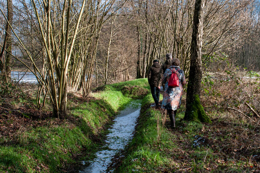 Eelco, Yvonne en Ivor (op de rug gezien) wandelen langs een beekloop op landgoed 't Medler