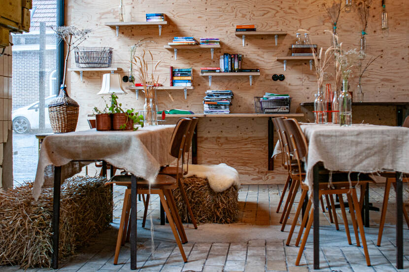 Interieur van de Suvelfabryk, tafels en stoelen met daaronder ook hooibalen en in de achtergrond een aantal boekenplanken.